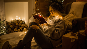 Christmas Book Flood, girl sitting in front of a fire reading a book. Welcome to Jólabókaflóðið a Modern Tradition.